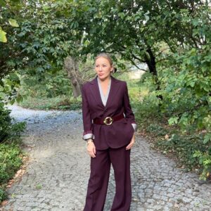 Izabela Kuligowska stylizka w bordowym garniturze z szerokimi spodniami i paskiem, stojąca na kamiennej ścieżce w parku, elegancka stylizacja jesienna.