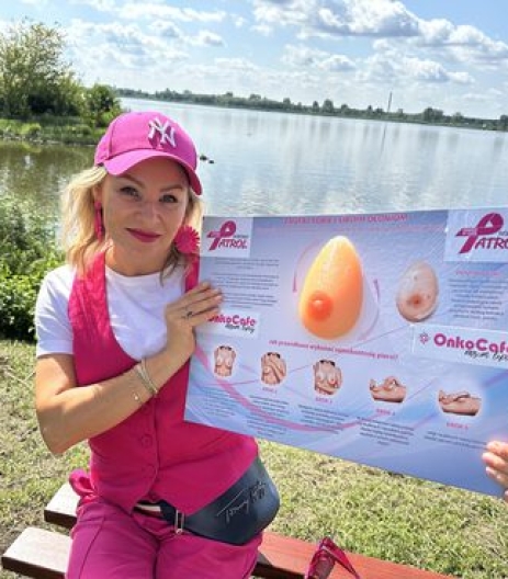 Izabela Kuligowska stylizka w różowym stroju i czapce, prezentująca materiały edukacyjne "Różowy Patrol" i OnkoCafe dotyczące samokontroli piersi, nad jeziorem, akcja profilaktyczna.