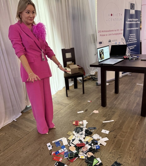 Izabela Kuligowska stylizka w fuksjowym garniturze z piórami, prezentująca metki z ubrań na podłodze, podczas eventu "Jak Cię widzą, tak Ci płacą", warsztaty wizerunkowe.